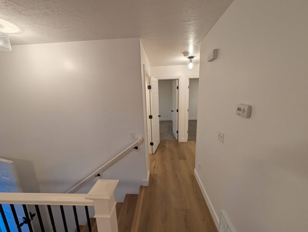 Finished hallway with wood-look flooring, white trim and stair railing in the Brigham City renovation